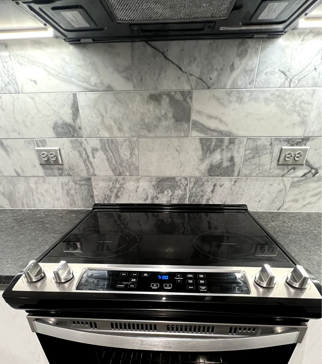 A kitchen with a cooktop and a marble backsplash.